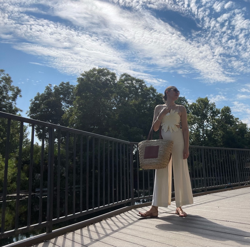 a woman n a white maxi skirt with a white flower crop top and  brown lace up sandals and a straw tote with leather pocket