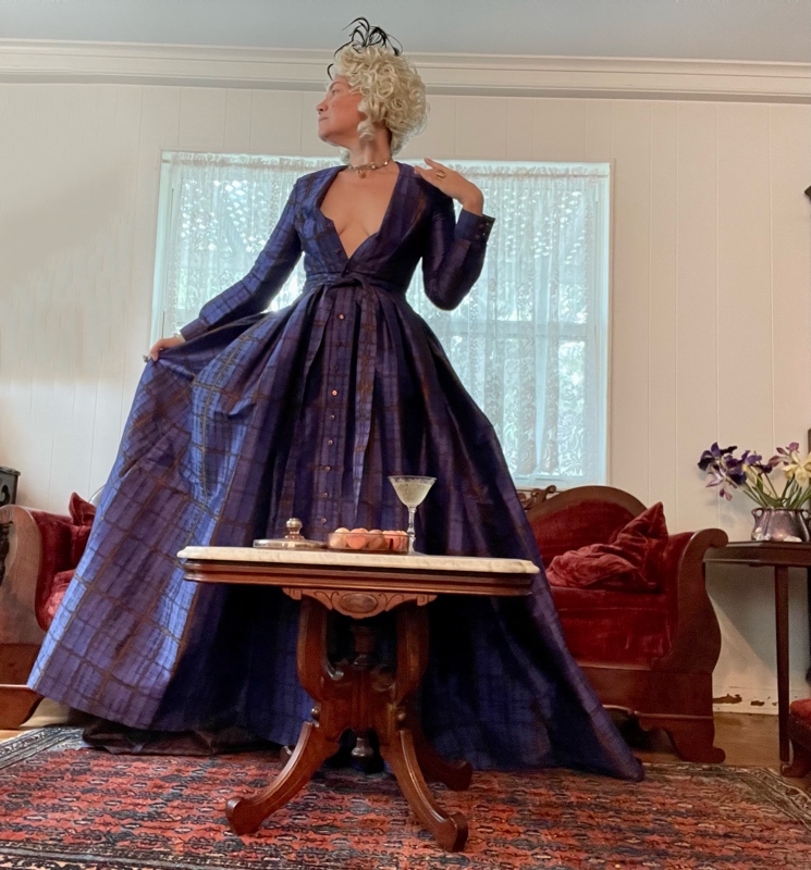 a woman in a Marie Antoinette Wig, plaid gown and jewels with a velvet couch, macaroons, and champagne