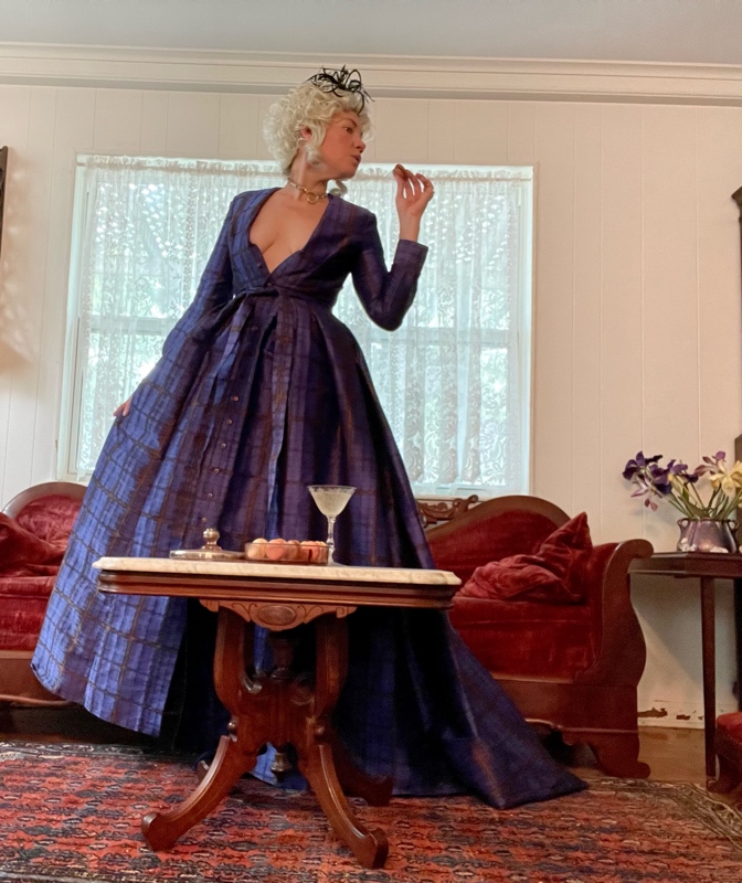a woman in a Marie Antoinette wig, plaid gown with a red velvet couch, maroons and champagne