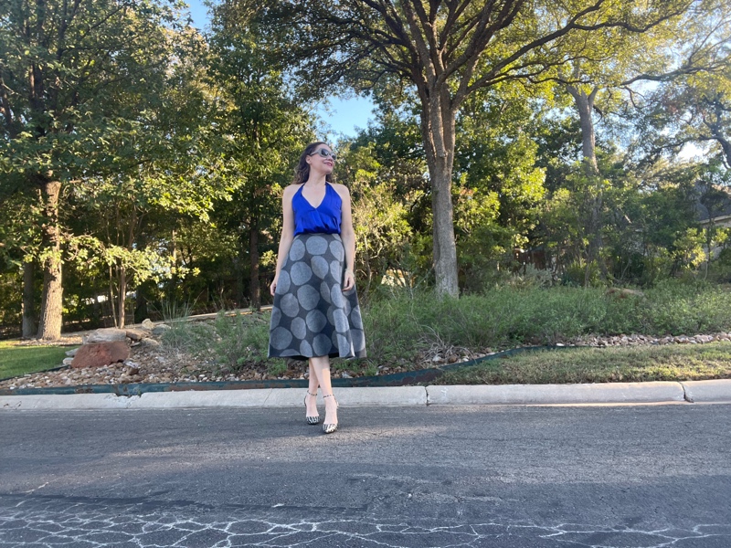 a woman in a blue silk halter top and a grey polka dot skirt with houndstooth wedges