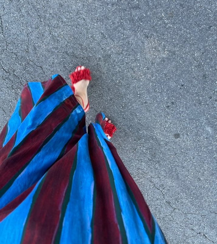 a woman in a blue and red striped skirt and turtleneck set with red fringe shoes and a leopard bag 