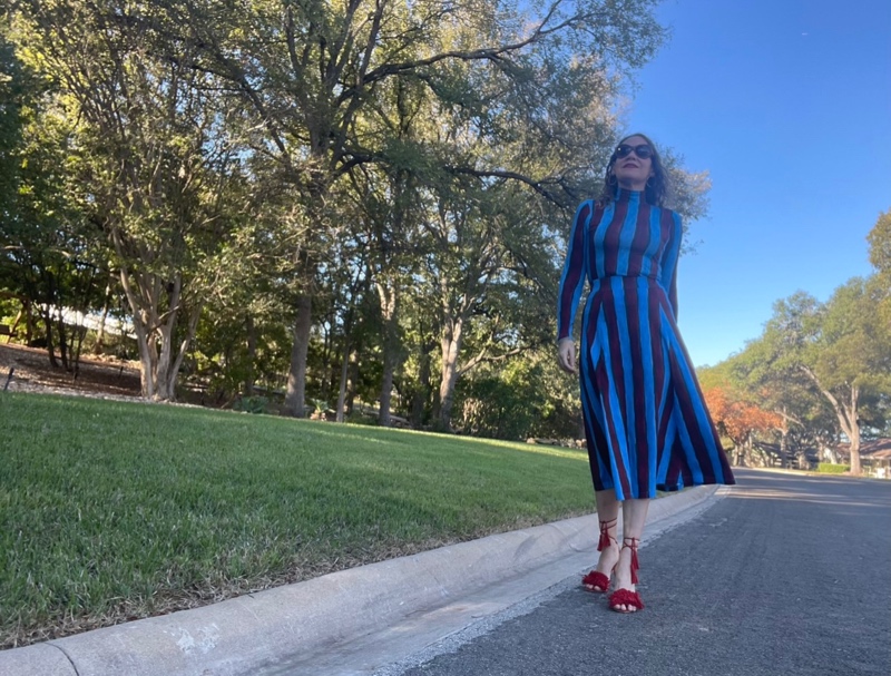 a woman in a blue and red striped skirt and turtleneck set with red fringe shoes and a leopard bag 