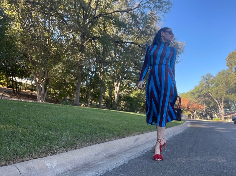 a woman in a blue and red striped skirt and turtleneck set with red fringe shoes and a leopard bag 