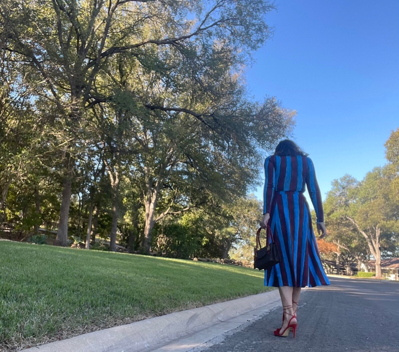 a woman in a blue and red striped skirt and turtleneck set with red fringe shoes and a leopard bag