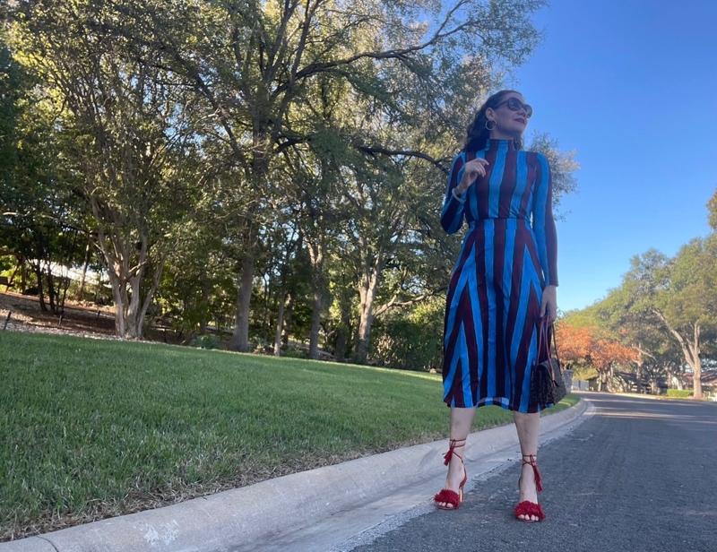 a woman in a blue and red striped skirt and turtleneck set with red fringe shoes and a leopard bag