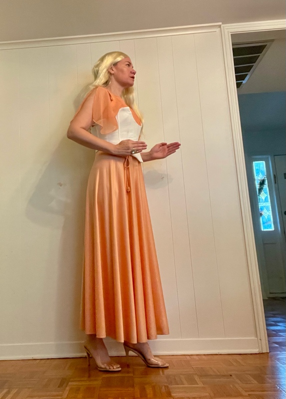 a woman in a peach dress with a white corset and a long blonde Wig