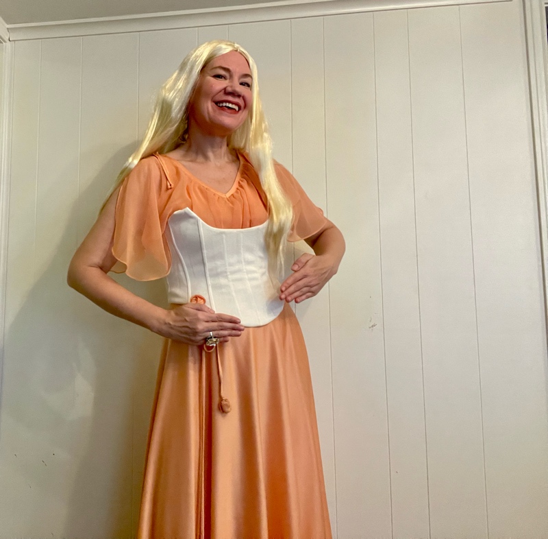 a woman in a peach dress with a white corset and a long blonde wig