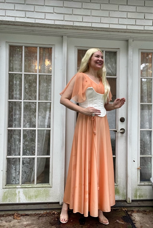 a woman in a peach dress and white corset with long blonde hair 