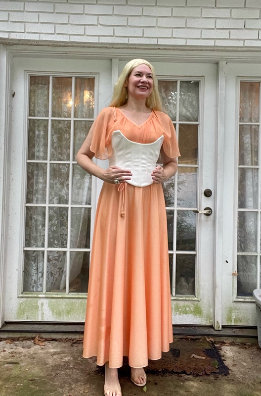 a woman in a peach dress with a white corset and long blonde wig