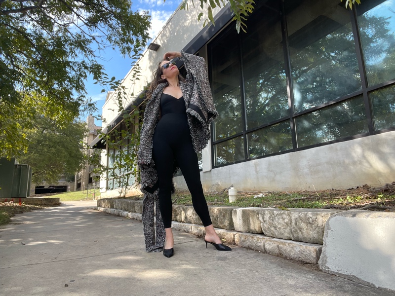 a woman in. black onesie and a tweed cape and black mules 