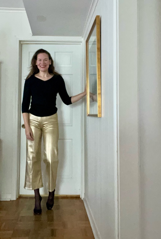 a woman in gold pants and a black sweater and black heels