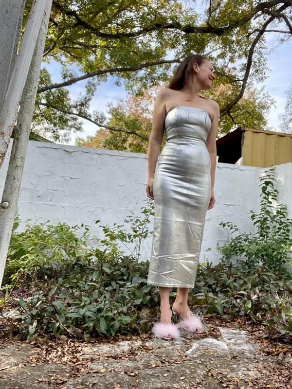 a woman in a silver strapless dress and pink feather shoes in a garden