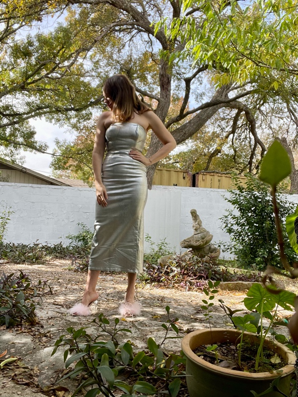 a woman in a silver dress with pink feathered shoes in a garden 