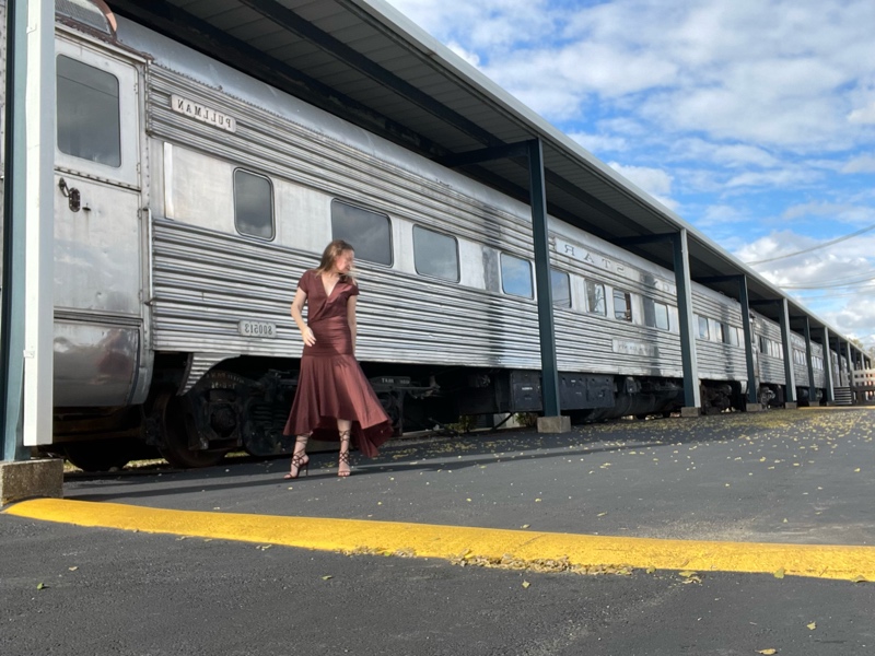 a woman in a brown dress and shoes in front of a train 