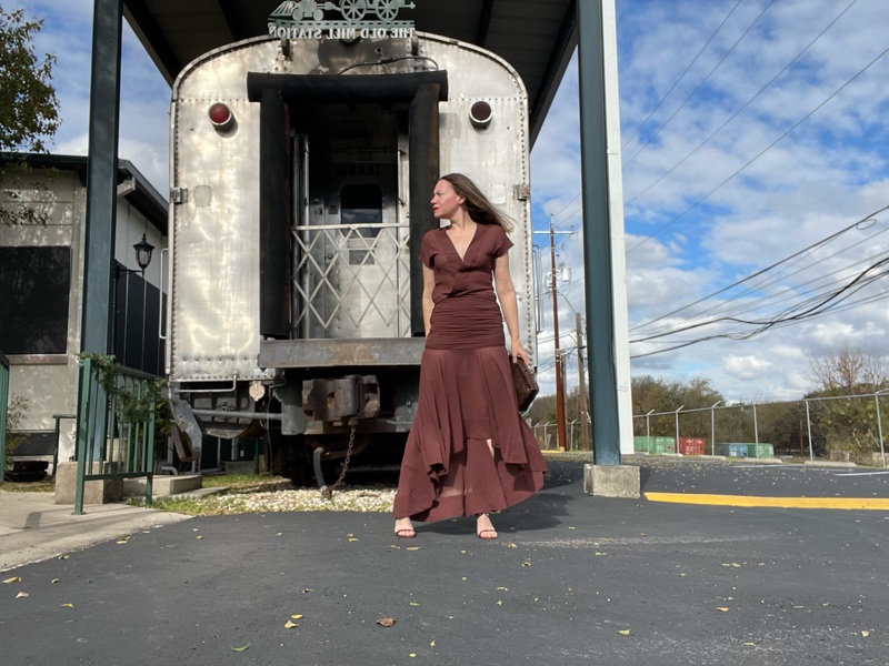 a woman in a brown dress and shoes in front of a train