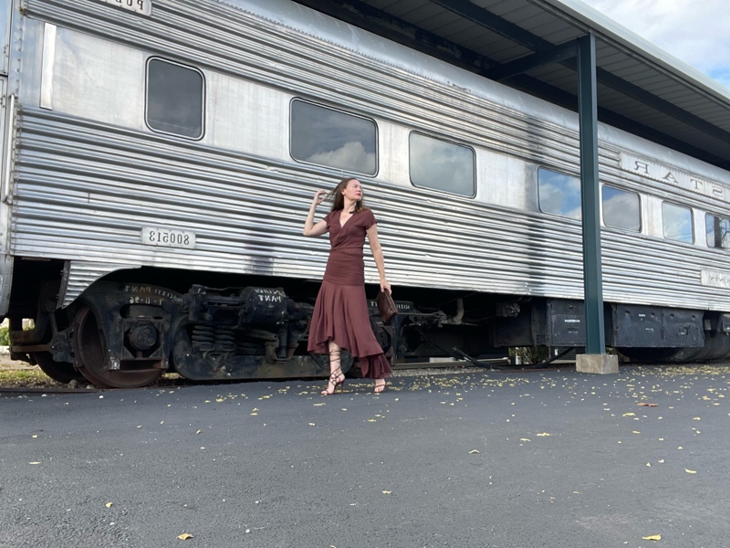 a woman in a brown dress and brown shoes in front of a train