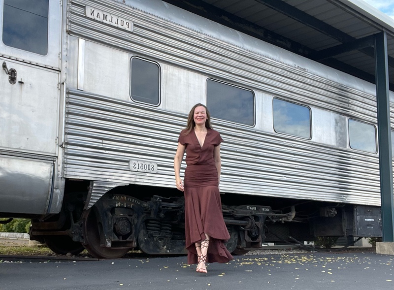 a woman in a brown dress in front of a train
