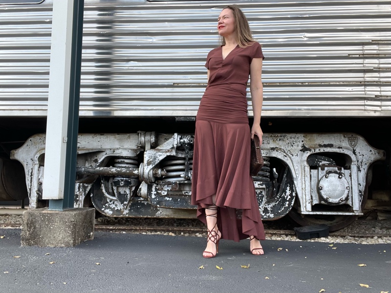 a woman in a brown dress in front of a train