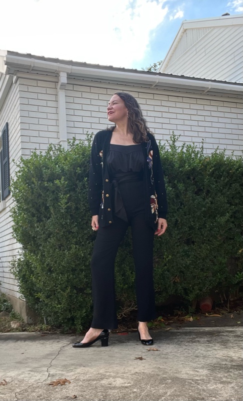a woman in black tank top, pants with tie, shoes and a black cardigan with sequin candy canes on it