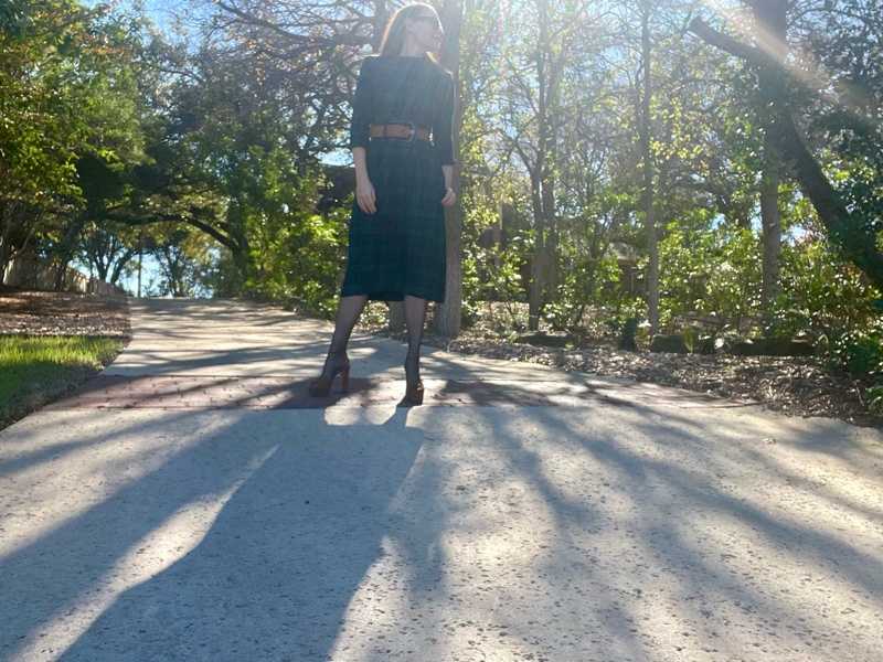 a woman in black watch plaid dress with a brown belt, black hose and brown suede platfroms