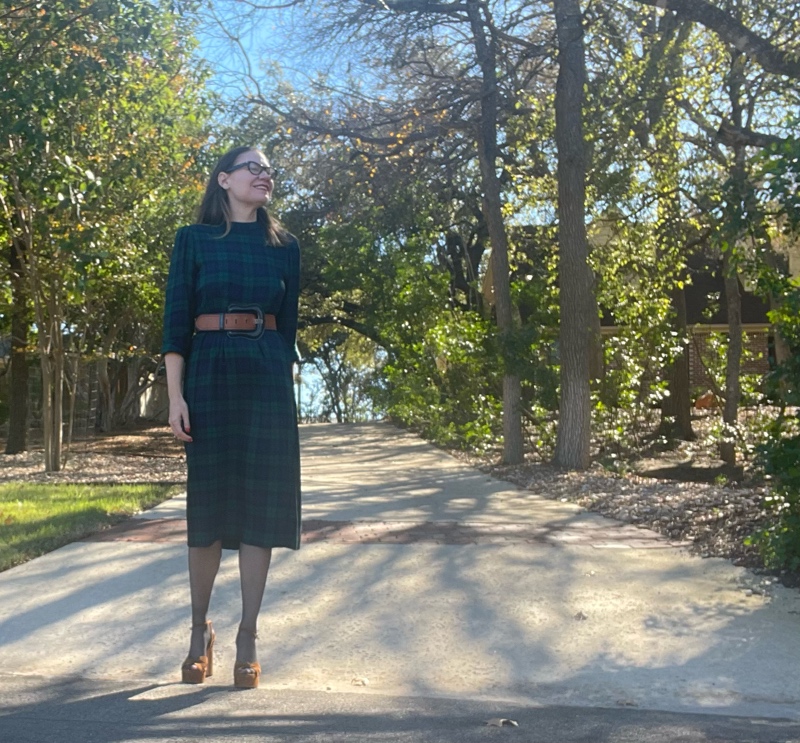 a woman in black watch plaid dress with a brown belt, black hose and brown suede platforms