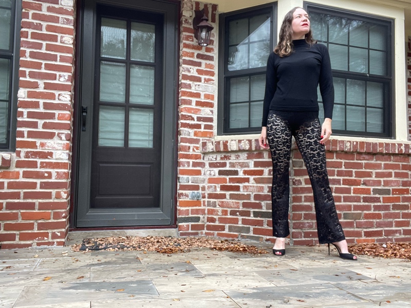 a woman in a black turtleneck, black sheer lace pants and black peep toe heels