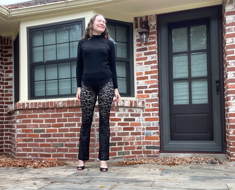 a woman in a black turtleneck, black sheer lace pants, and black peep toe heels