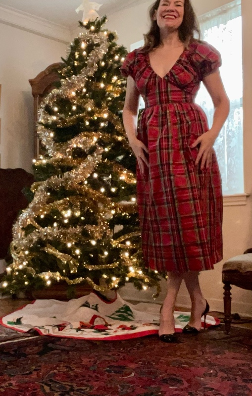 a woman in a plaid dress by a Christmas Tree