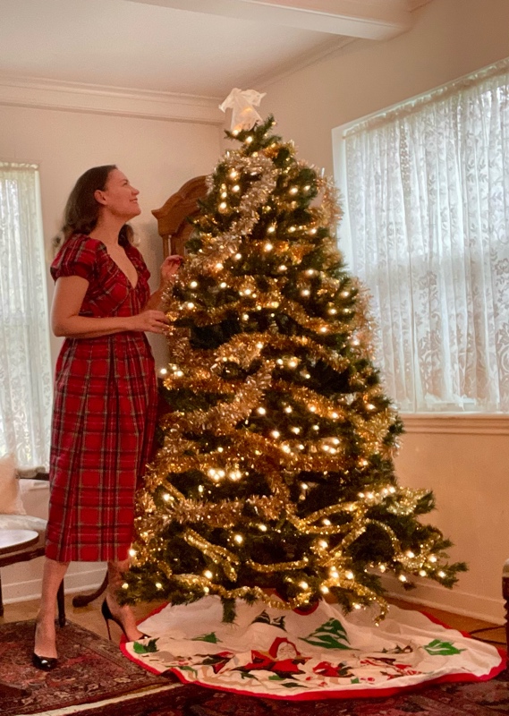 A woman in plaid dress and black heels by a Christmas Tree