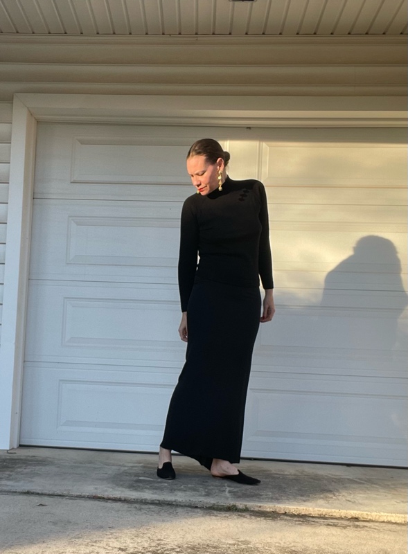 a woman in a black maxi skirt and turtleneck with mules and statement earrings 