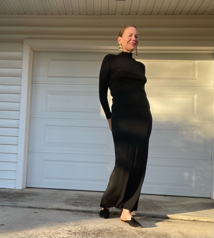 a woman in black maxi skirt and black turtleneck, mules and statement earrings