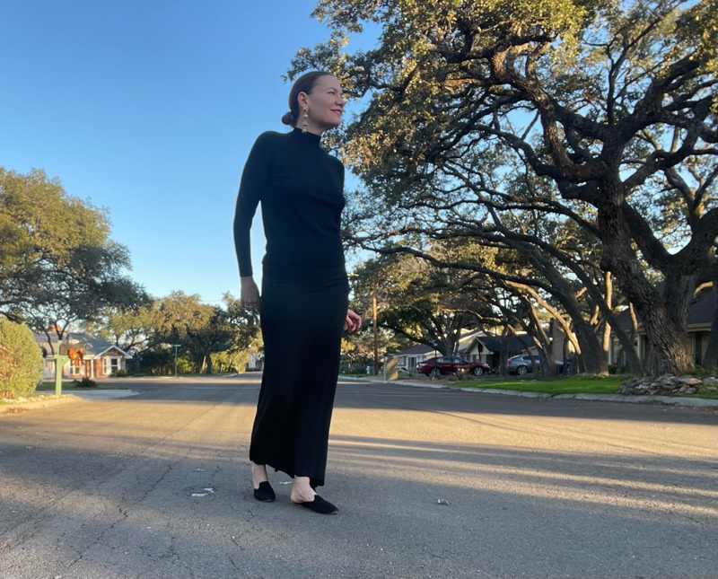 a woman in black maxi skirt, black turtleneck, black mules and statement earrings