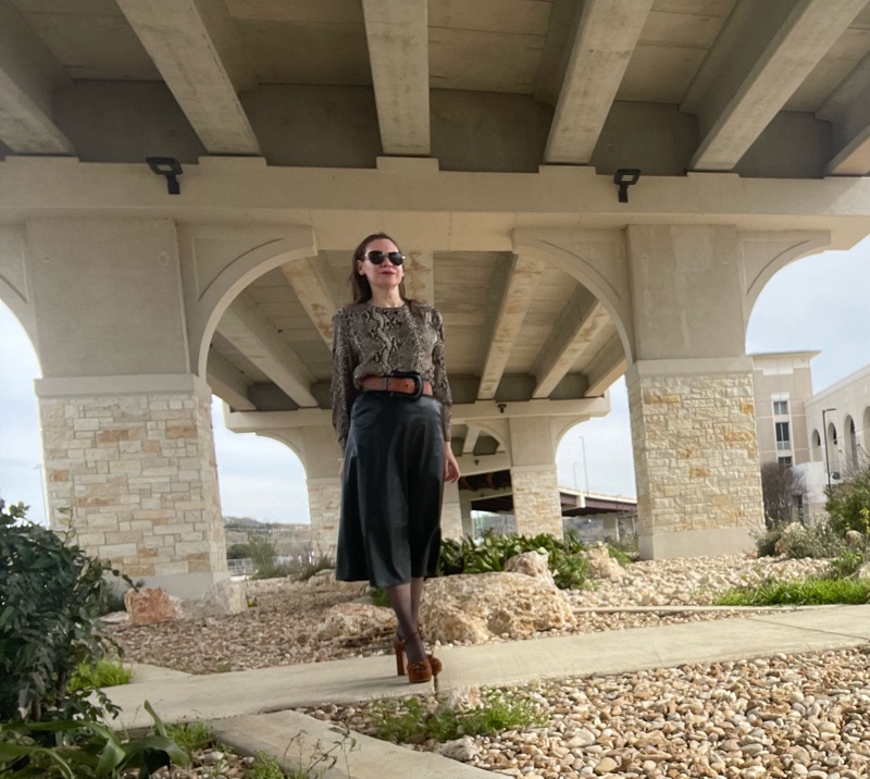 a woman in a silk snake print shirt, black leather skirt, hose, brown belt and brown suede platforms