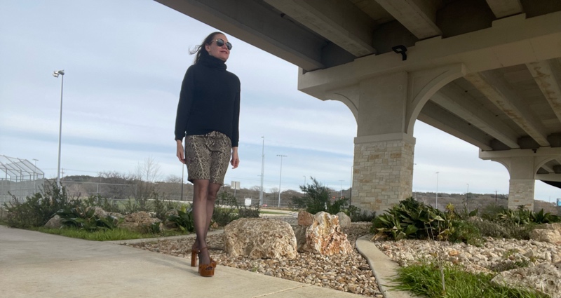 a woman in a black turtleneck sweatshirt, snake print silk skirt, black hose and brown suede platforms