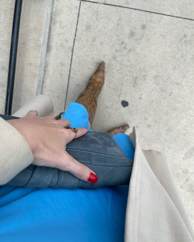 a woman in ablue slip dress, snakeskin boots, tan coat, and blue clutch