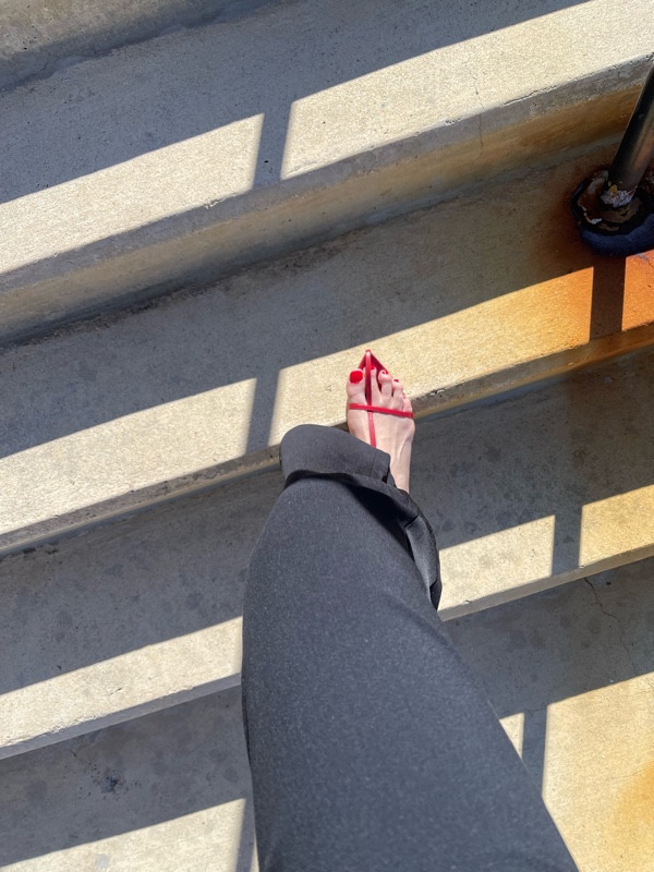 a woman's foot with red nails wand a red  cage Sandal and black jumpsuit on stairs