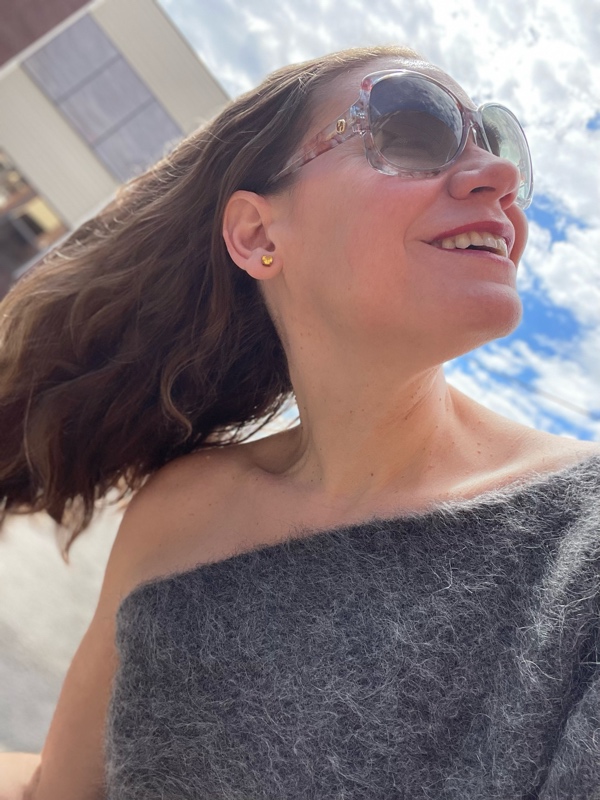 a close up of a woman in sunglasses and a one shoulder grey sweater