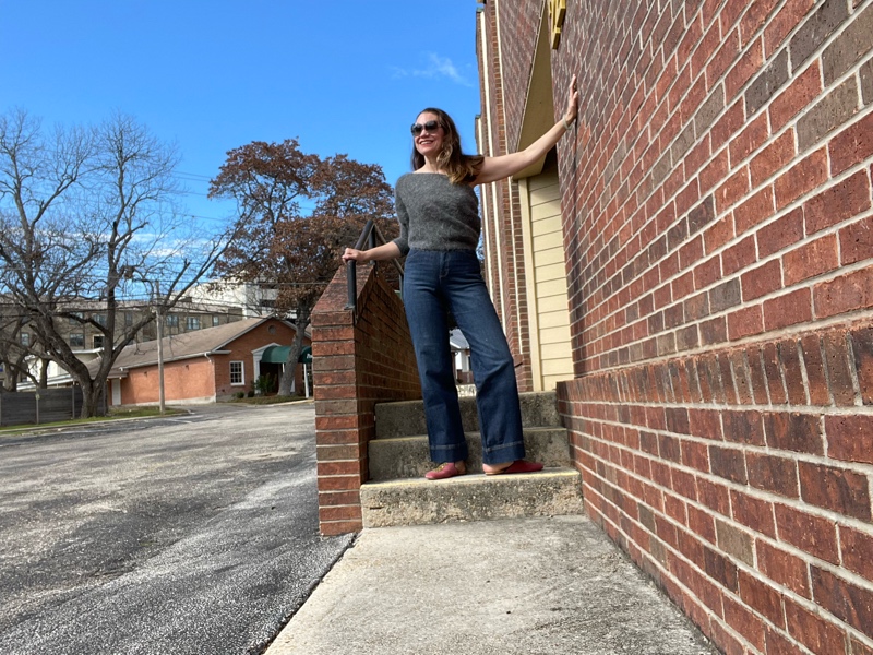 a woman in jeans and a grey one shoulder sweater and pink mules