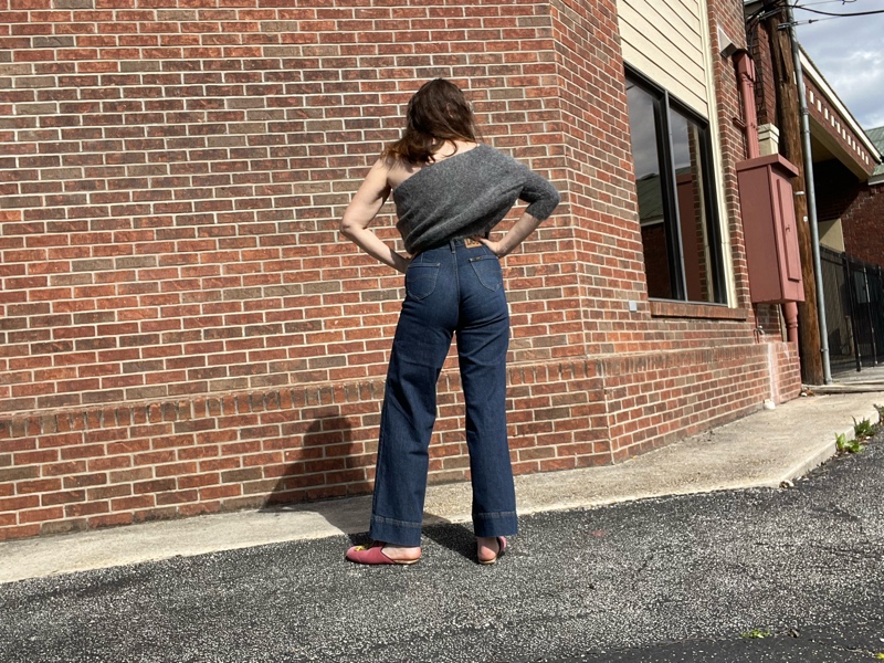 a woman in jeans and a grey one shoulder sweater with pink mules