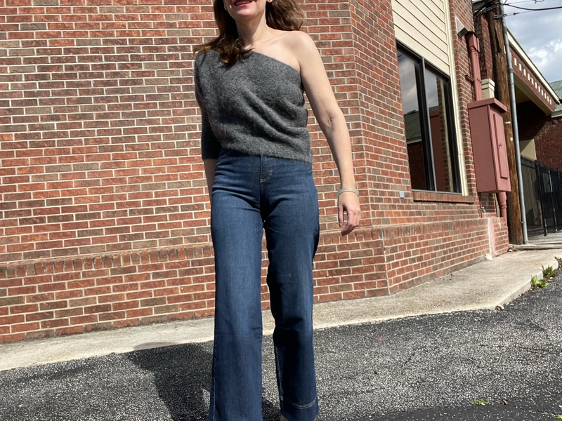 a woman in jeans and a grey one shoulder sweater with pink mules