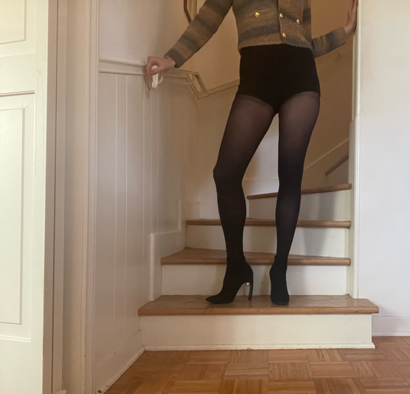 a woman on stairs in hose, short shorts, a cardigan and boots with a pearl on the arch