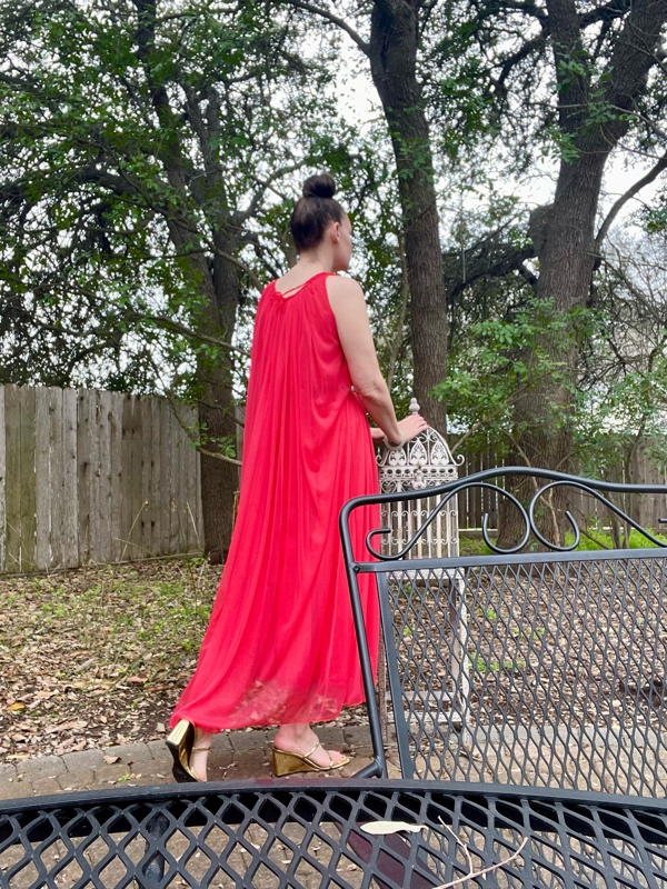 a woman in a pleated red nightgown with a tie at the waist and a bit of a cape in gold wedges 
