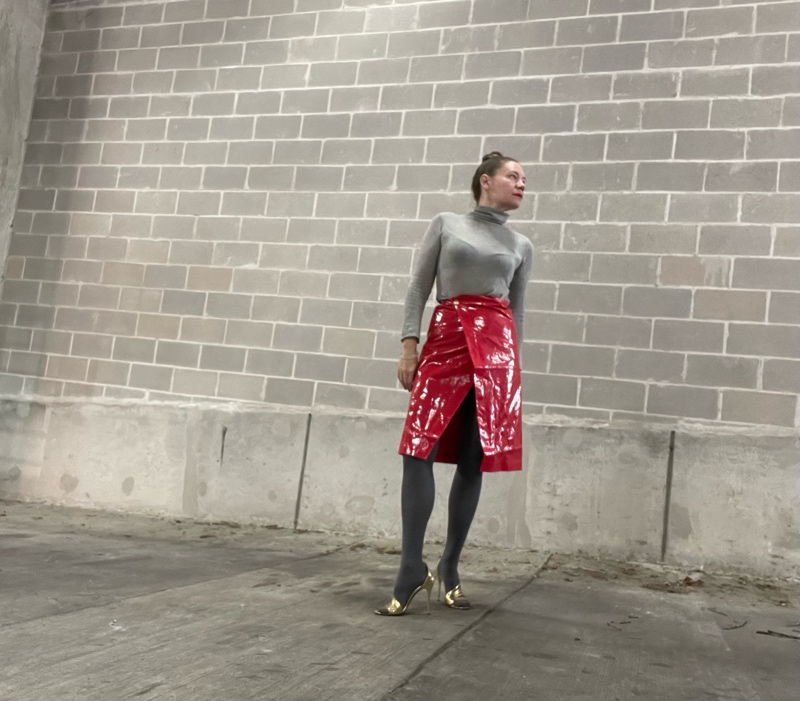a woman in a red laminated skirt with a grey turtleneck and great tights and gold heels