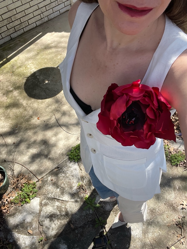 a woman in a white vest and a red floral brooch with white and denim chino mix  pants with white heels 