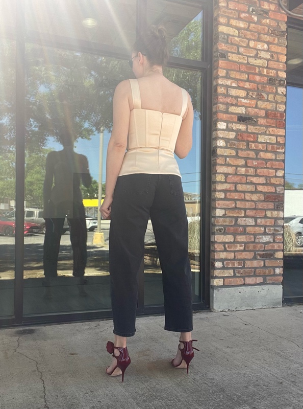 a woman in curved black jeans with a cream corset top with tassels and red stripy rose sandals