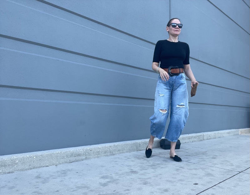 a woman in balloon jeans, a black tee and a belt and black suede mules
