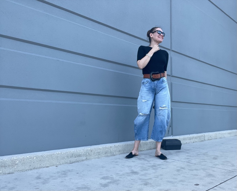 a woman in balloon jeans a black tee and an oversized belt with black suede mules