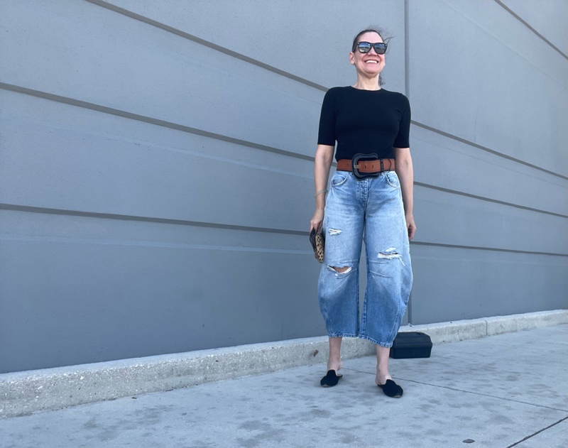 a woman in balloon jeans with a black tee and an oversized belt and black suede mules 