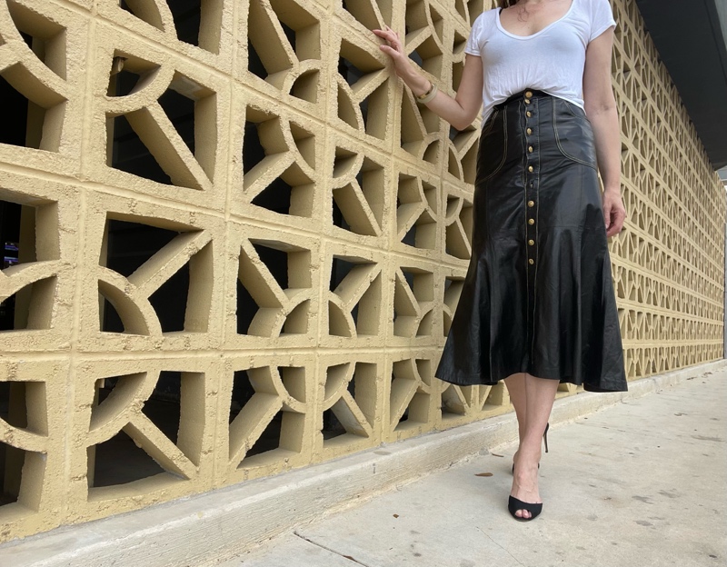 a woman in a Roberto Cavalli leather skirt with gold buttons, a white tee shirts and black sandal pumps