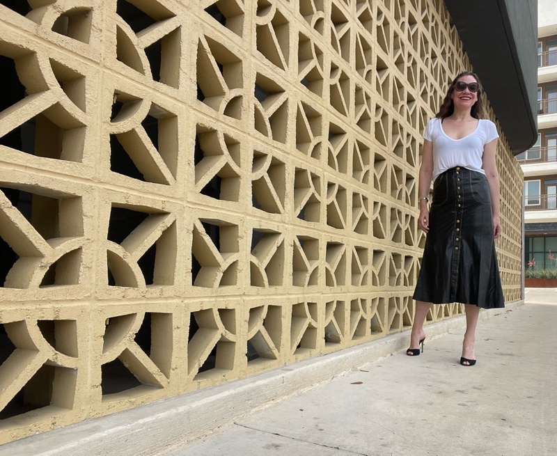 a woman in a Roberto Cavalli leather skirt with gold buttons, a white tee shirts and black sandal pumps